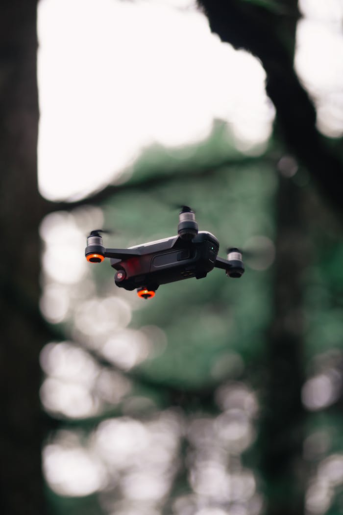 A sleek drone captured mid-flight among trees, emphasizing aerial technology outdoors.