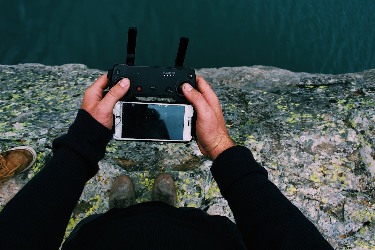 A person holding a drone remote control with a smartphone attached, standing on a rocky surface.